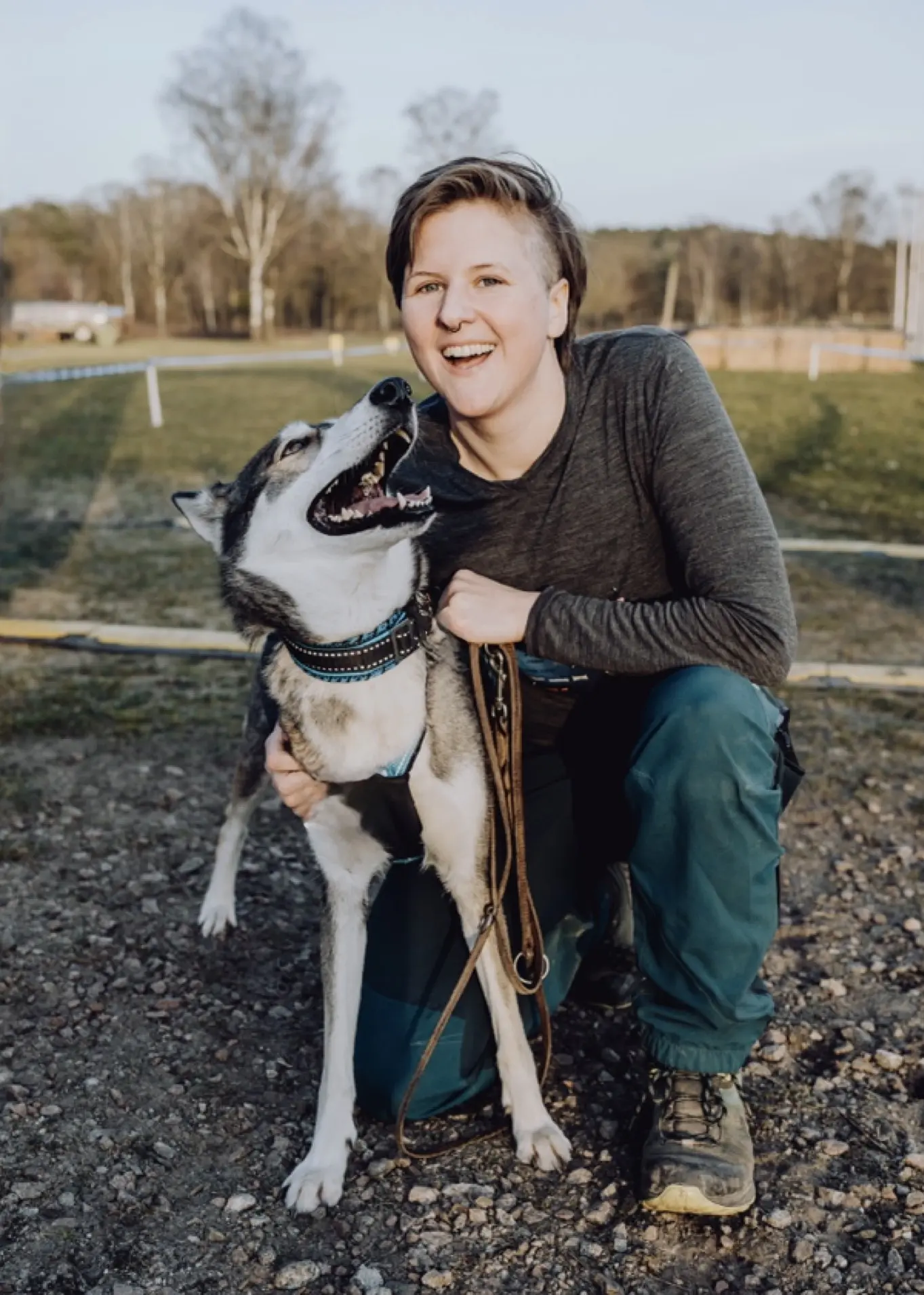 Frau in einer schwarzen Jacke mit Kapuze auf hält einen weißen kleinen Hund auf dem Arm